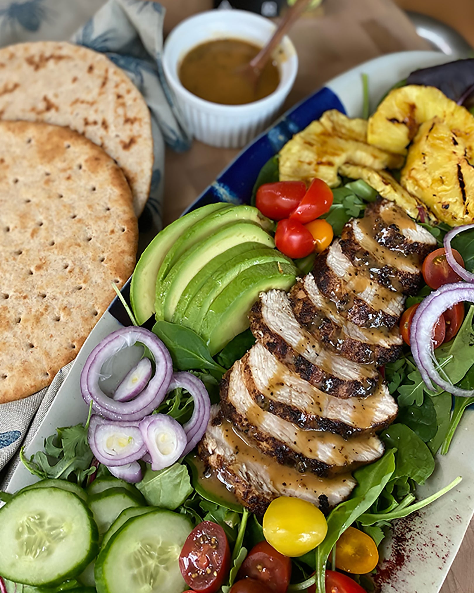 Sliced chicken on salad with pita on the side